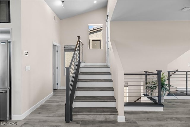 staircase with baseboards, high vaulted ceiling, and wood finished floors