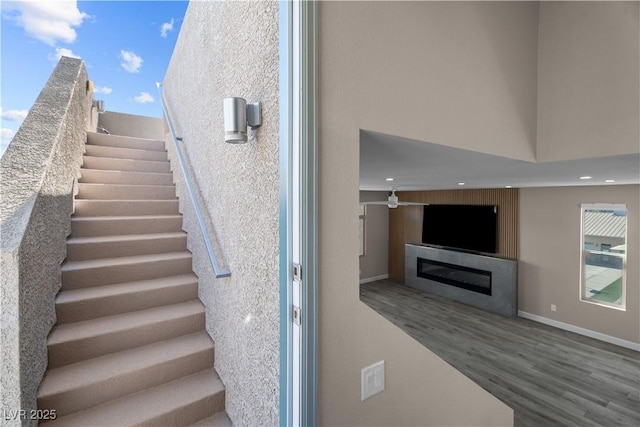 stairway with a glass covered fireplace, recessed lighting, baseboards, and wood finished floors