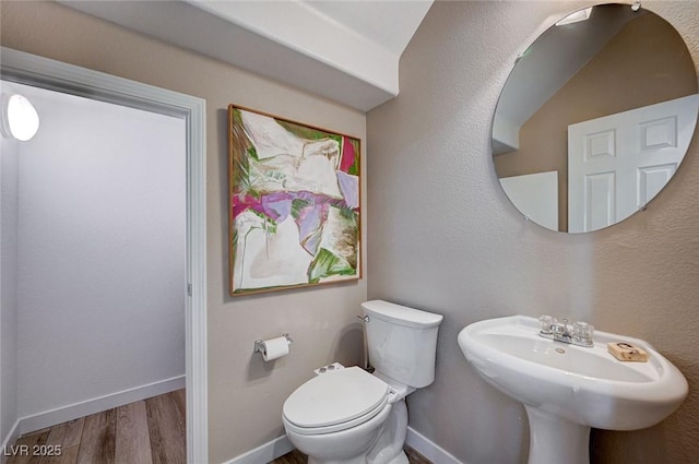 bathroom with toilet, wood finished floors, baseboards, and a sink