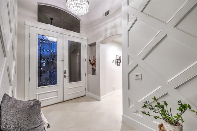 foyer with visible vents, baseboards, a chandelier, light tile patterned floors, and arched walkways