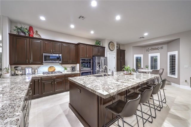 kitchen featuring a breakfast bar area, a center island with sink, visible vents, a sink, and appliances with stainless steel finishes