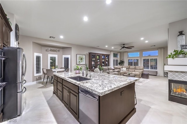 kitchen with visible vents, dark brown cabinets, a center island with sink, stainless steel appliances, and a sink