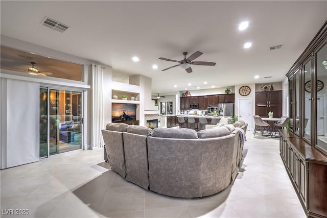 living room with visible vents, recessed lighting, a ceiling fan, and a glass covered fireplace