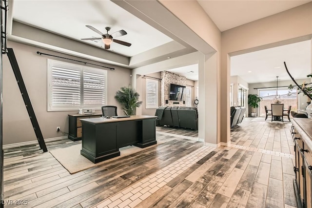 office with baseboards, light wood-style floors, a ceiling fan, and a raised ceiling