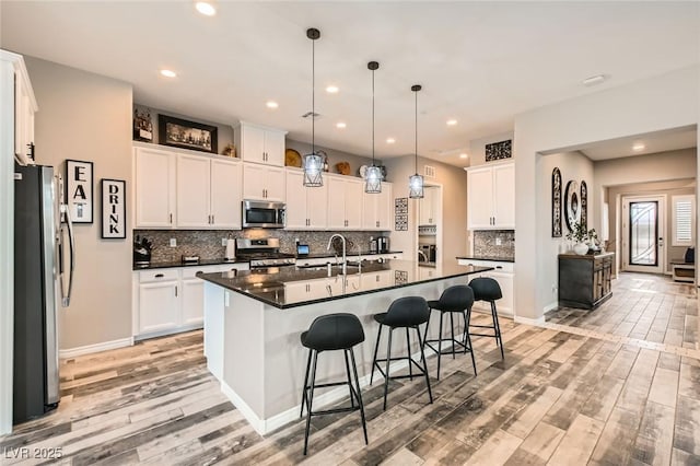 kitchen featuring a sink, a kitchen breakfast bar, dark countertops, stainless steel appliances, and light wood-style floors