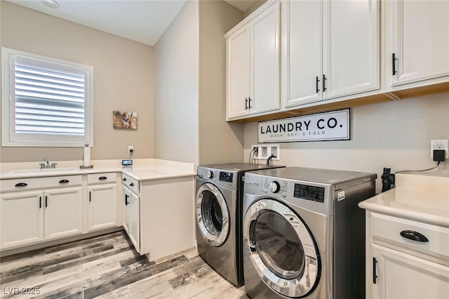 clothes washing area with washer and dryer, cabinet space, light wood finished floors, and a sink