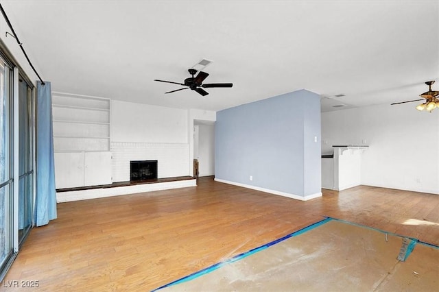 unfurnished living room featuring visible vents, a ceiling fan, built in features, wood finished floors, and a brick fireplace