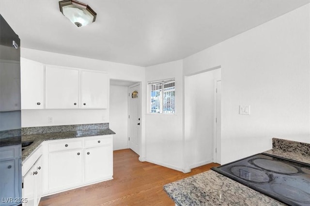 kitchen featuring dark stone countertops, light wood-style flooring, and white cabinetry