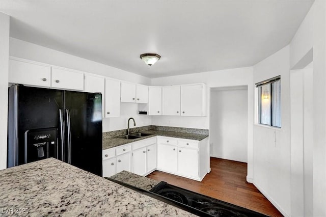 kitchen featuring dark stone countertops, dark wood-style flooring, a sink, white cabinetry, and black refrigerator with ice dispenser