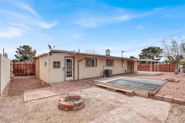 rear view of house with cooling unit, a patio, a fenced backyard, and an outdoor fire pit