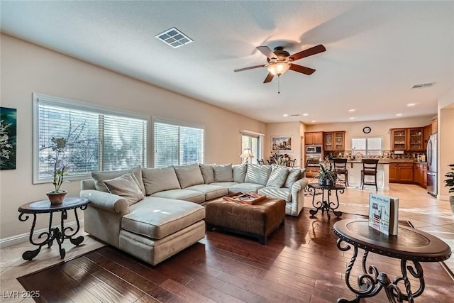 living room featuring light wood-type flooring, visible vents, baseboards, and ceiling fan