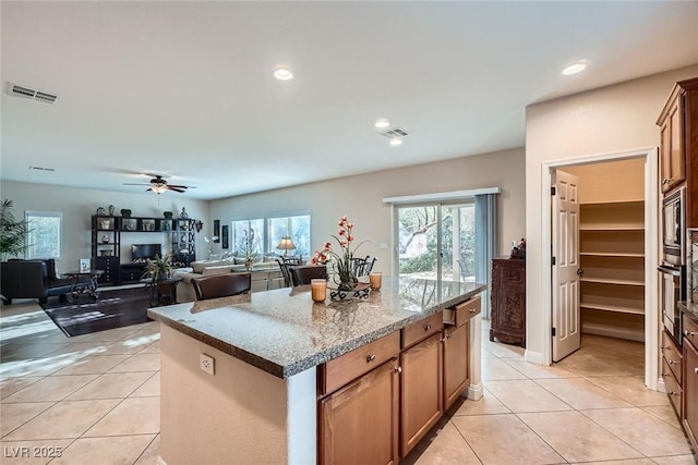 kitchen with light tile patterned floors, visible vents, built in microwave, and a kitchen island