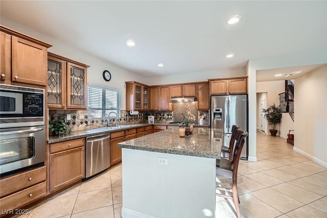 kitchen featuring under cabinet range hood, a sink, stainless steel appliances, light tile patterned floors, and decorative backsplash