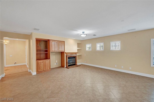 unfurnished living room with a glass covered fireplace, built in shelves, and baseboards