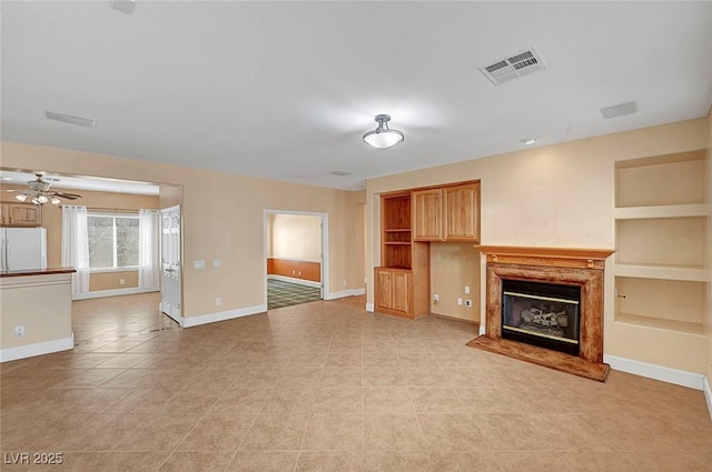 unfurnished living room featuring built in shelves, baseboards, visible vents, a premium fireplace, and ceiling fan