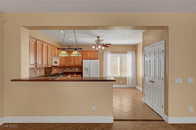 kitchen featuring white appliances, a peninsula, ceiling fan, dark countertops, and tasteful backsplash