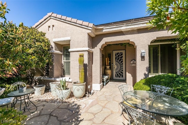 doorway to property with stucco siding, a patio, outdoor dining space, and a tiled roof