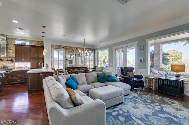 living room with a wainscoted wall, visible vents, crown molding, a chandelier, and dark wood-style flooring