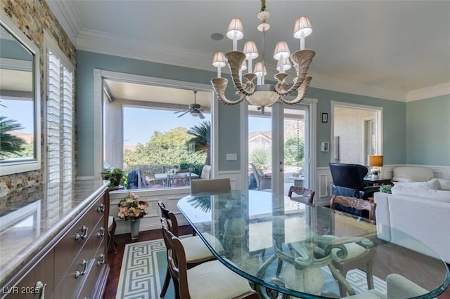 dining room with a wainscoted wall, ornamental molding, ceiling fan with notable chandelier, french doors, and dark wood-style floors