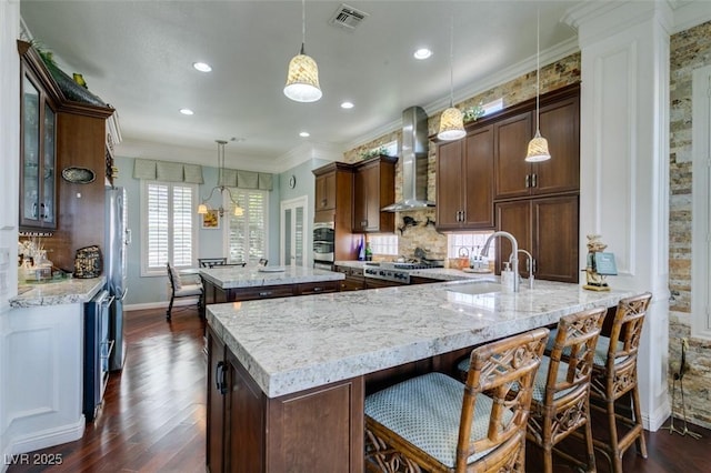 kitchen featuring visible vents, a kitchen island, wall chimney range hood, dark wood-style floors, and a sink