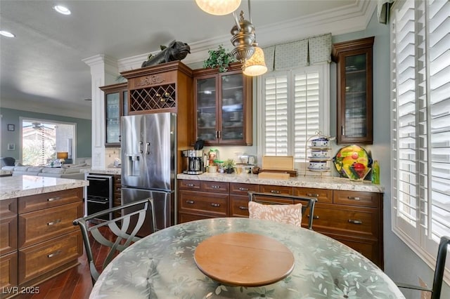 kitchen with stainless steel refrigerator with ice dispenser, wood finished floors, crown molding, glass insert cabinets, and light stone countertops