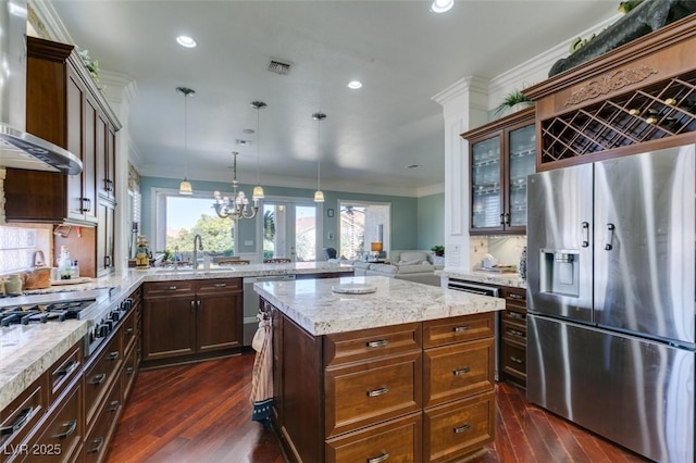 kitchen featuring visible vents, a peninsula, a sink, stainless steel appliances, and wall chimney exhaust hood