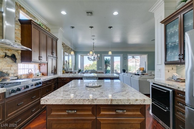 kitchen with wall chimney range hood, stainless steel gas cooktop, open floor plan, ornamental molding, and a peninsula