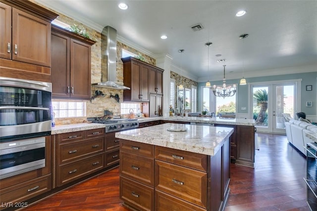 kitchen featuring a peninsula, ornamental molding, stainless steel appliances, wall chimney exhaust hood, and a center island