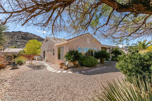 view of property exterior featuring a tiled roof, fence, a mountain view, and stucco siding