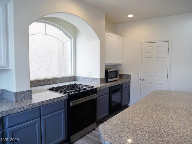 kitchen featuring blue cabinetry, stainless steel microwave, gas range oven, white cabinets, and tile counters