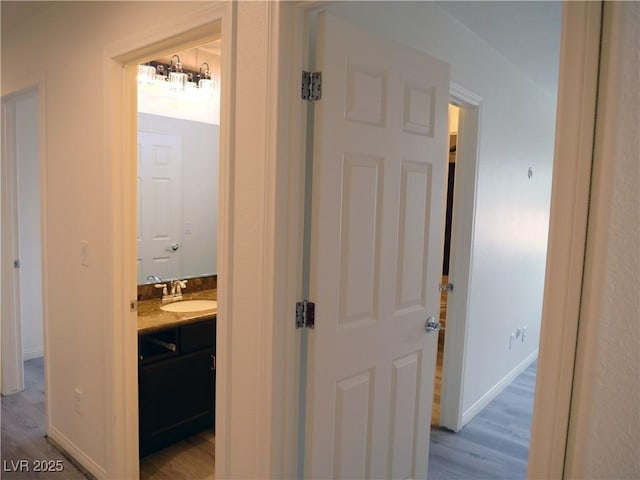 hallway featuring light wood-style flooring, baseboards, and a sink