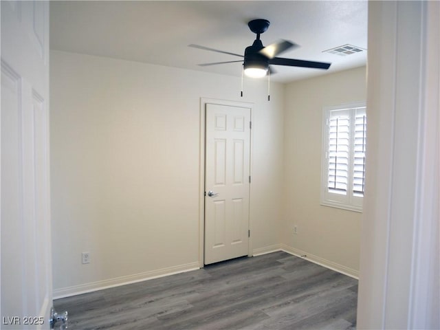 unfurnished room with dark wood-style floors, visible vents, baseboards, and a ceiling fan