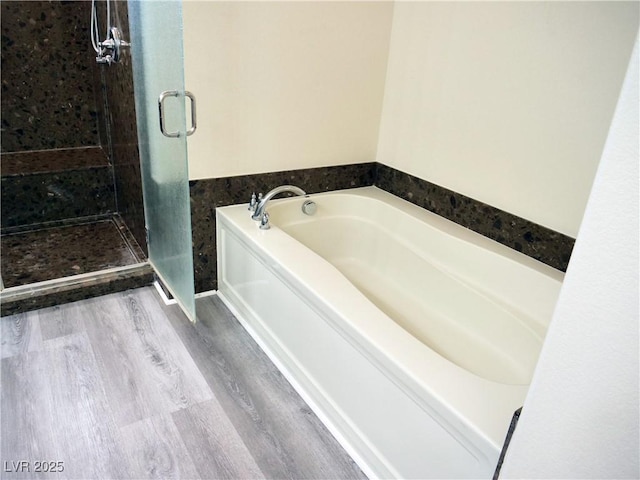 full bathroom featuring a shower stall, a bath, and wood finished floors