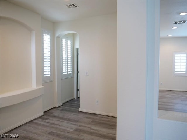 interior space with arched walkways, visible vents, baseboards, and wood finished floors