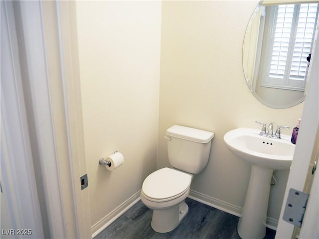 half bathroom with toilet, wood finished floors, and baseboards