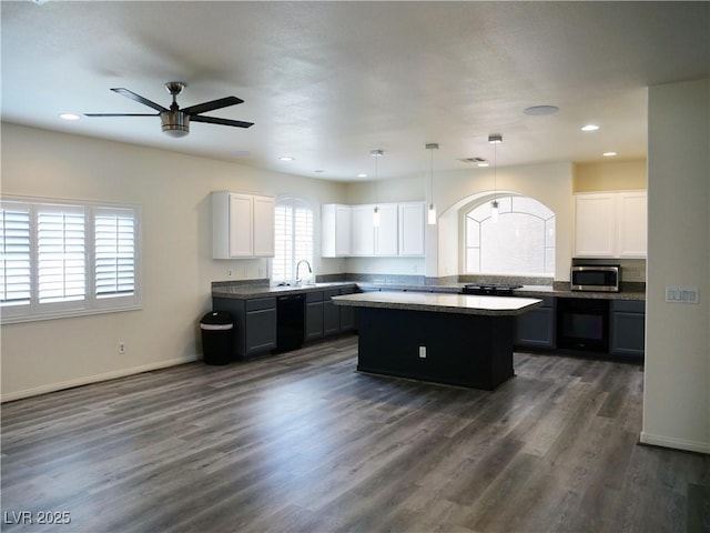 kitchen with a ceiling fan, a kitchen island, dark wood finished floors, a sink, and stainless steel microwave