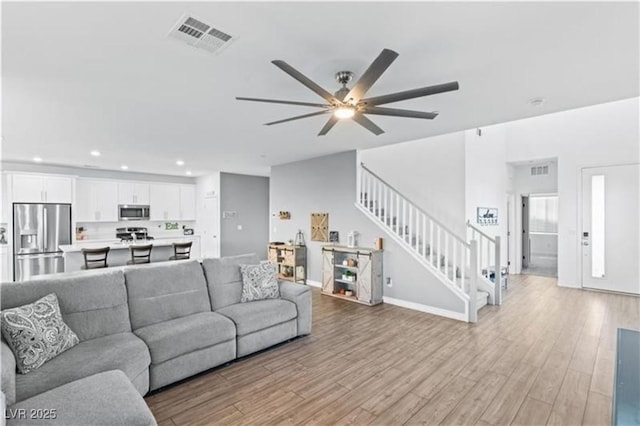 living room featuring stairway, visible vents, light wood-style flooring, recessed lighting, and ceiling fan