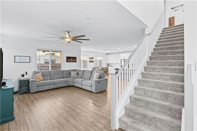 living area with recessed lighting, a ceiling fan, wood finished floors, and stairs