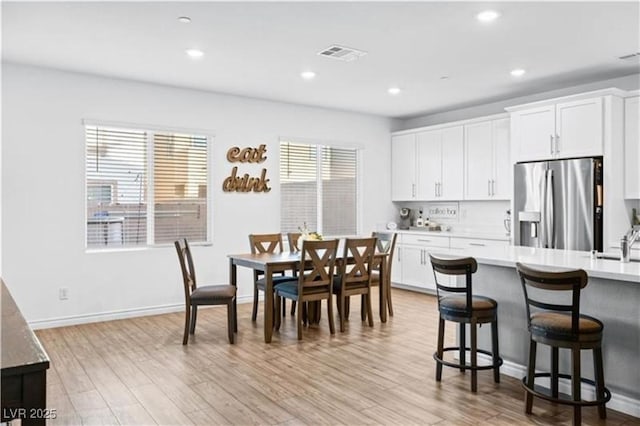 kitchen with a breakfast bar, light wood-style flooring, visible vents, and stainless steel fridge