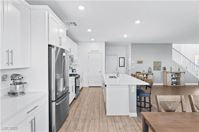 kitchen featuring visible vents, light wood-type flooring, a sink, a kitchen breakfast bar, and stainless steel appliances