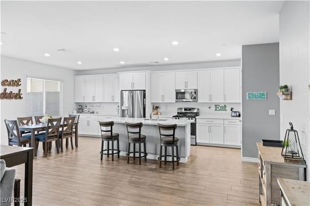 kitchen featuring a breakfast bar area, white cabinets, light wood-type flooring, and appliances with stainless steel finishes