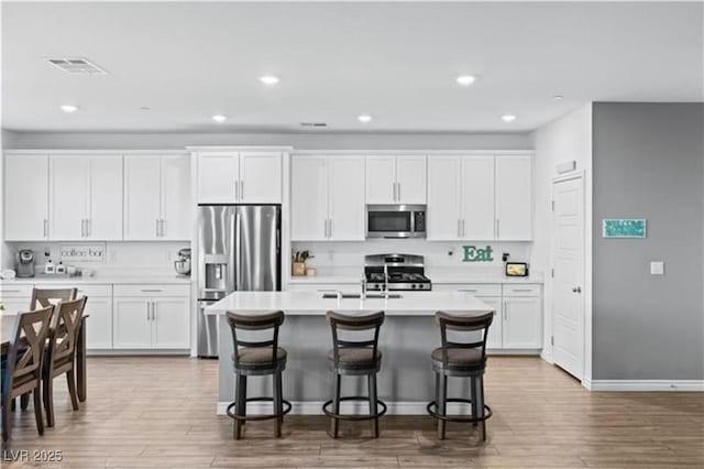 kitchen with white cabinets, a kitchen breakfast bar, stainless steel appliances, and light countertops