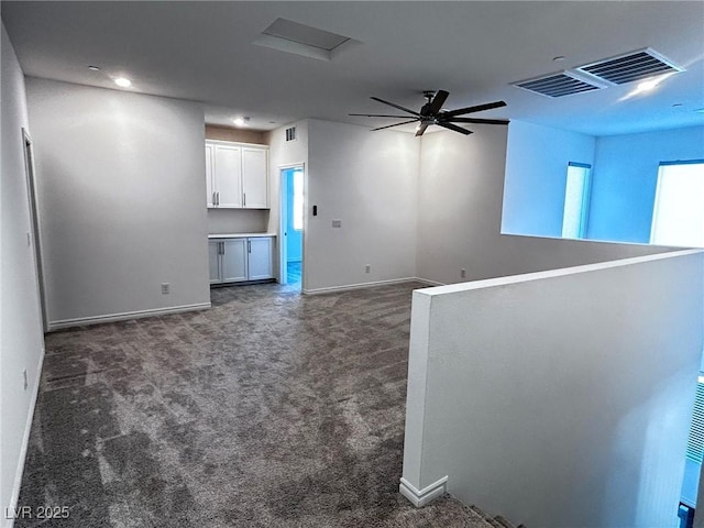 empty room with dark carpet, baseboards, ceiling fan, and visible vents