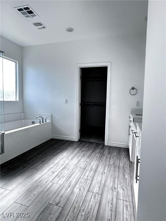 bathroom with visible vents, a bath, a walk in closet, vanity, and wood finished floors
