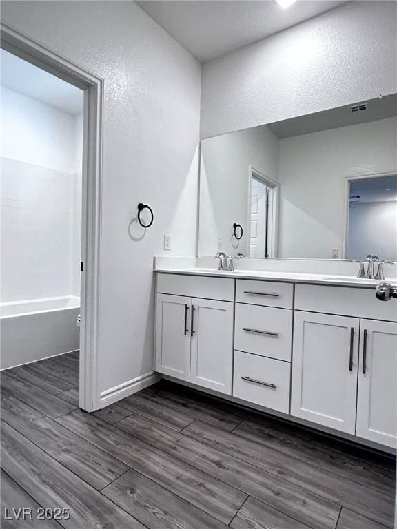 bathroom with a textured wall, a sink, double vanity, and wood finished floors
