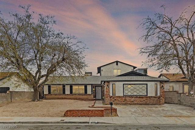 view of front facade featuring fence, brick siding, and stucco siding