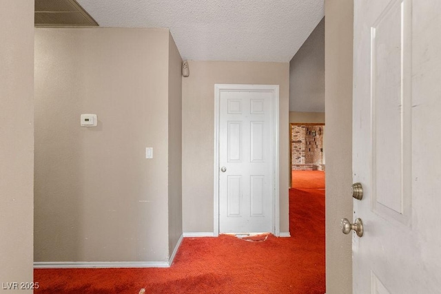 hall with carpet flooring, visible vents, a textured ceiling, and baseboards