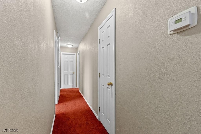 corridor featuring carpet flooring, a textured ceiling, baseboards, and a textured wall