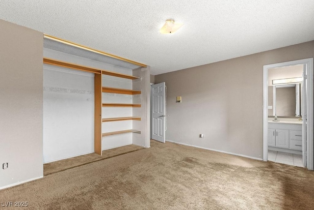 unfurnished bedroom with connected bathroom, carpet flooring, a closet, a textured ceiling, and a sink