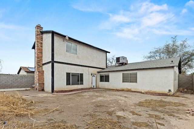 back of house featuring stucco siding, central AC, a chimney, and fence